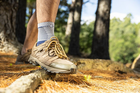 Man hiking in the woods. The shot focuses on his hiking shoes and the MalleoTrain ankle brace he's wearing, which is great for relieving pain from injuries and conditions like arthritis