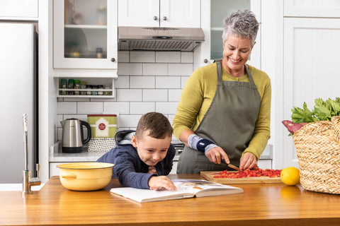 Older woman cooking with her son. She is chopping vegetables while wearing a ManuTrain wrist brace, a great support for relieving tendonitis wrist pain