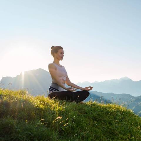 Woman sitting on a hill meditating wearing a Bauerfeind back brace.