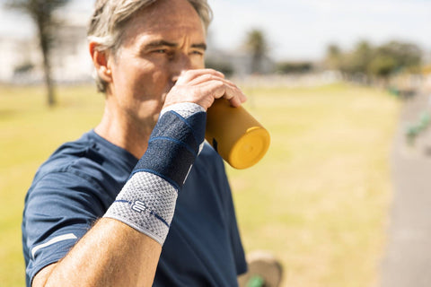 Older man at the park drinking water. He is wearing Bauerfeind's ManuTrain wrist brace to help alleviate wrist pain 