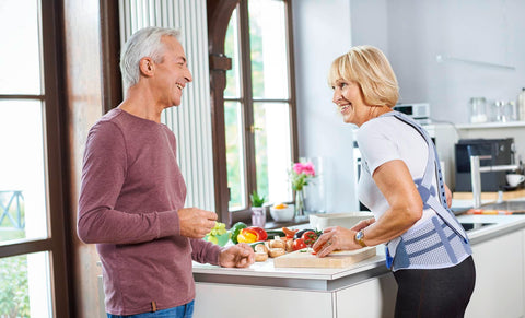 Two people laughing and talking in the the kitchen, one wearing a Bauerfeind back brace for Dowager's hump