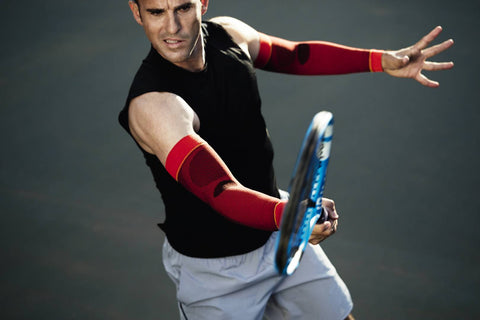 Action shot of a tennis player swinging his racket. He's wearing Bauerfeind's red Sports Compression Arm Sleeves to boost circulation and improve overall sports recovery