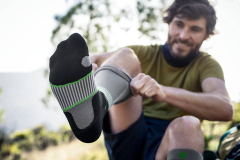 Shot of a man pulling on Bauerfeind's Outdoor Compression Socks. The shot focuses on the underside of the sock on his foot to show this sports compression sock's different support zones