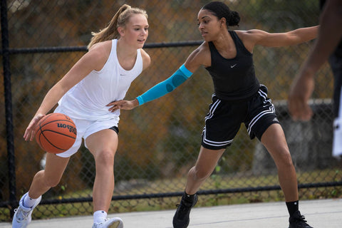 Two female basketball players training. They're both wearing loose clothing and one is wearing Bauerfeind's Sports Compression Arm Sleeve, good gear for avoiding muscle fatigue 