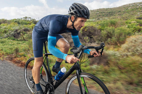 Man cycling aerodynamically, keeping good form and wearing Bauerfeind's Sports Compression Arm Sleeves to improve his cycling speed