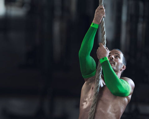 Man climbing a rope at the gym as part of his workout. He's wearing Bauerfeind's Sports Arm Compression sleeves to minimise fatigue as he climbs