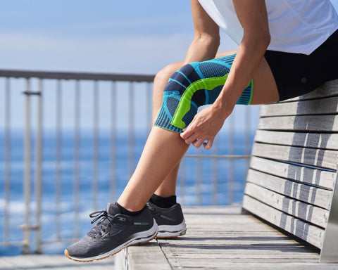 woman sitting on a bench at the beach pulling on Bauerfeind's Sports Knee Brace