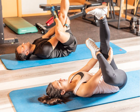 Man and woman at the gym doing a figure 4 stretch for the hips and glutes