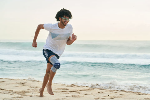 Man running on the beach in a GenuTrain Knee Brace to avoid knee pain