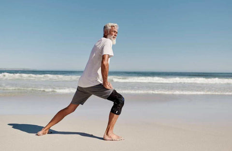 Man on the beach doing a lunge in Bauerfeind's GenuTrain OA Knee Brace