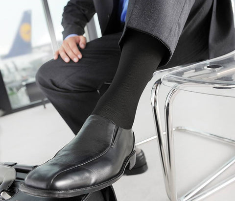 Man in business attire sitting in an airport lounge. He is wearing Bauerfeind's VenoTrain Men's Business Compression Socks for his travels.