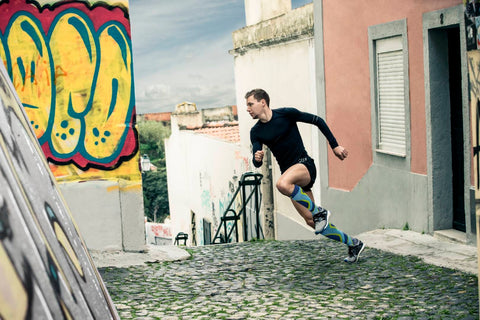 Man running in between buildings, past a wall covered in colourful graffiti. He's wearing Bauerfeind's Performance Socks, perfect for boosting endurance while marathon training