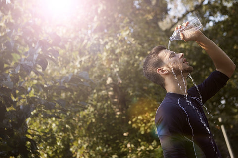 Man standing in a park pouring bottled water onto his face. Hydration is key to maximising performance in sports