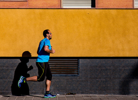 Man running near an orange building. He has good running form with a mid foot strike underneath his torso, great for minimising and preventing ankle pain when running