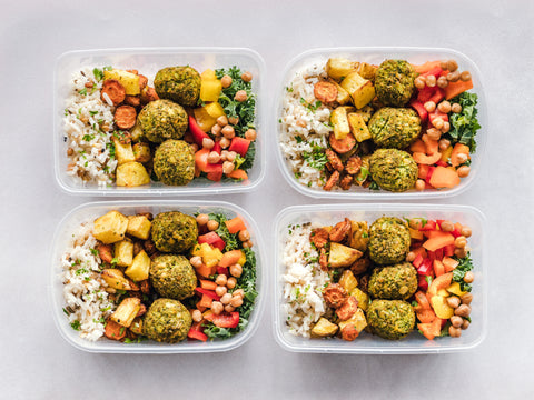 Overhead shot of four clear lunch boxes filled with rice, baked potato slices, meatballs, and fresh salad, great basketball training meals