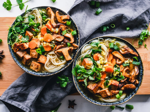 Overhead shot of two bowls of noodles topped with carrots, parsley, leeks, mushrooms, and squash - good and hearty winter meals
