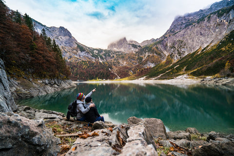 A couple taking a break from walking looking at a clear lake surrounded by mountains