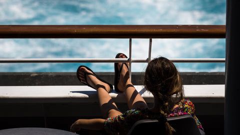 Girl relaxing on a balcony. She's facing away from the camera, sitting on a deck chair, and has propped her feet up on the balcony rails.