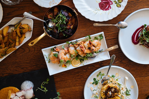 Overhead shot of food on a wooden table. They include prawns and various plates of roasted and fresh vegetables, great nutrition for improving athletic performance 