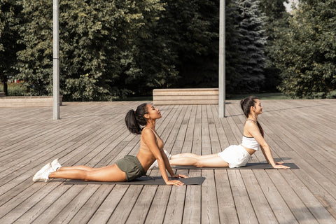 Two women out on the deck arching upward into a cobra stretch. The exercise relaxes ab, chest, and hip muscles, making it a great cool down oprion