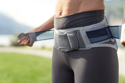 Woman putting on Bauerfeind's SacroLoc Back Brace to relieve back pain on her jogs