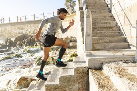 Man running up the stairs from a beach wearing Bauerfeind's Performance Compression Socks