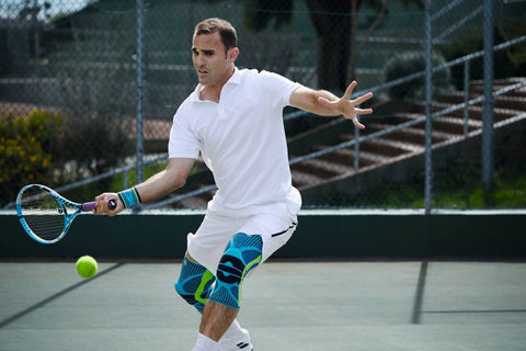 Man training in tennis. He is hitting a forehand shot. He's wearing Bauerfeind's Sports Knee Support and Sports Wrist Strap