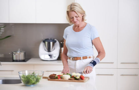 Woman wearing Buaerfeind's ManuTrain Wrist brace while cooking in the kitchen to manage wrist arthritis pain