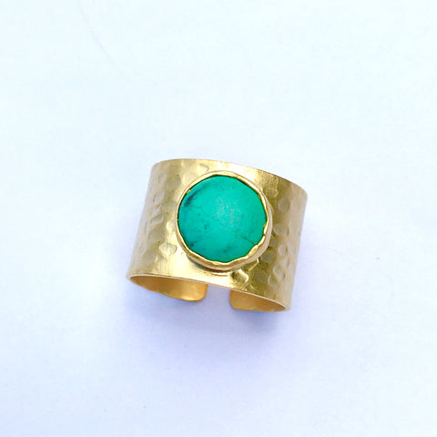 gold colored thick band made of brass with hammered design and turquoise round circular stone set in the middle of this adjustable sized ring that is made in turkey.