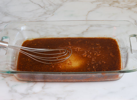 Image of the soy sauce, lime juice, vegetable oil, sugar, cumin, chili powder, and garlic all mixed together in a rectangular glass pyrex dish for the oven.
