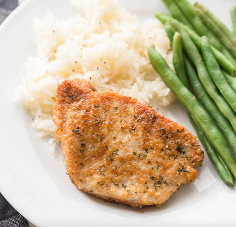 Image of a parmesan crusted pork chop on a plate with mashed potatoes and green beans.