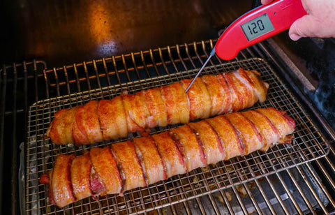 Image of backstraps on the smoker with the author measuring the temperature with a meat thermometer.