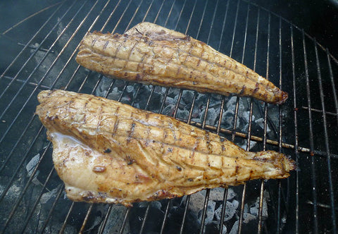 Image of two redfish half-shells cooking on the grill aboive hot coals.