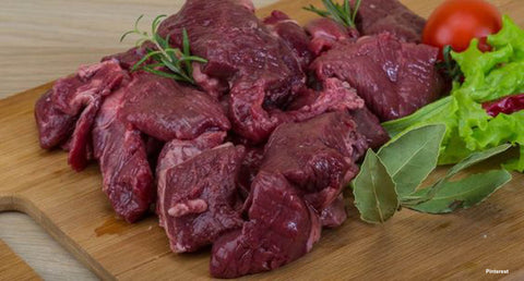 Image of raw venison steak pieces piled on a cutting board prior to cutting.