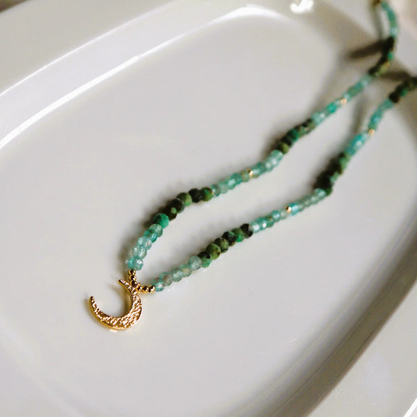A necklace with a blue string and gold moon at the bottom of it.