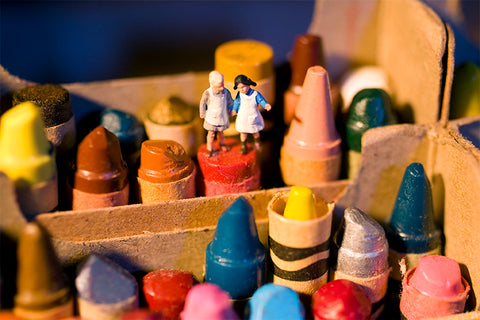 miniature figures exploring a colorful box of crayons