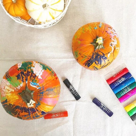 Kwik Stix pumpkin painting fall activity on a linen tablecloth with a small basket of real pumpkins in the frame