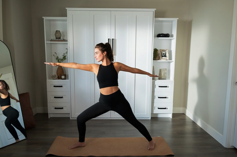 A woman gracefully practicing yoga in front of a mirror, with a murphy bed in the background.