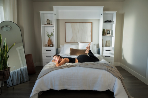 A woman relaxing on a murphy bed in a bedroom.