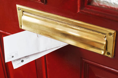Two envelopes poke out of a polished brass post box on a red door.