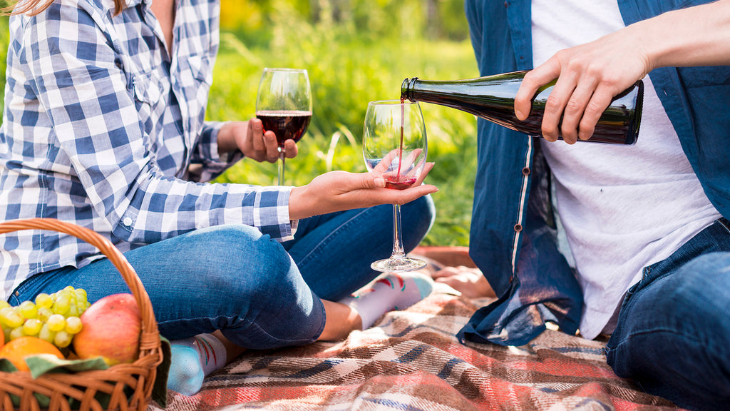 Dve osobe na pikniku u sumi nazdravljaju casom vina