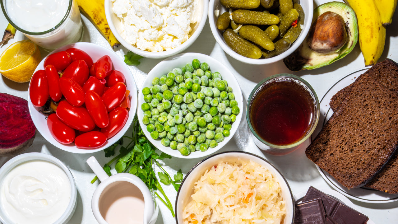 Dishes of peas, baby tomatoes, pickles amd yogurt in amongst regular healthy foods to demonstrate how easy it is adding probiotics to your meals.