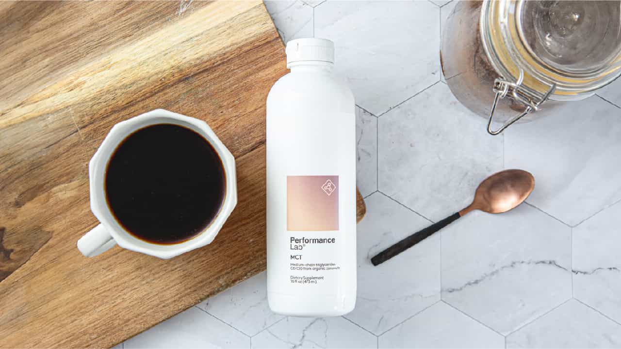 Best Organic MCT Oil to buy in 2024: Performance Lab® MCT Energy Oil bottle next to a cup of coffee on a wood cutting board and a copper spoon on a hexagonal marble tile counter.