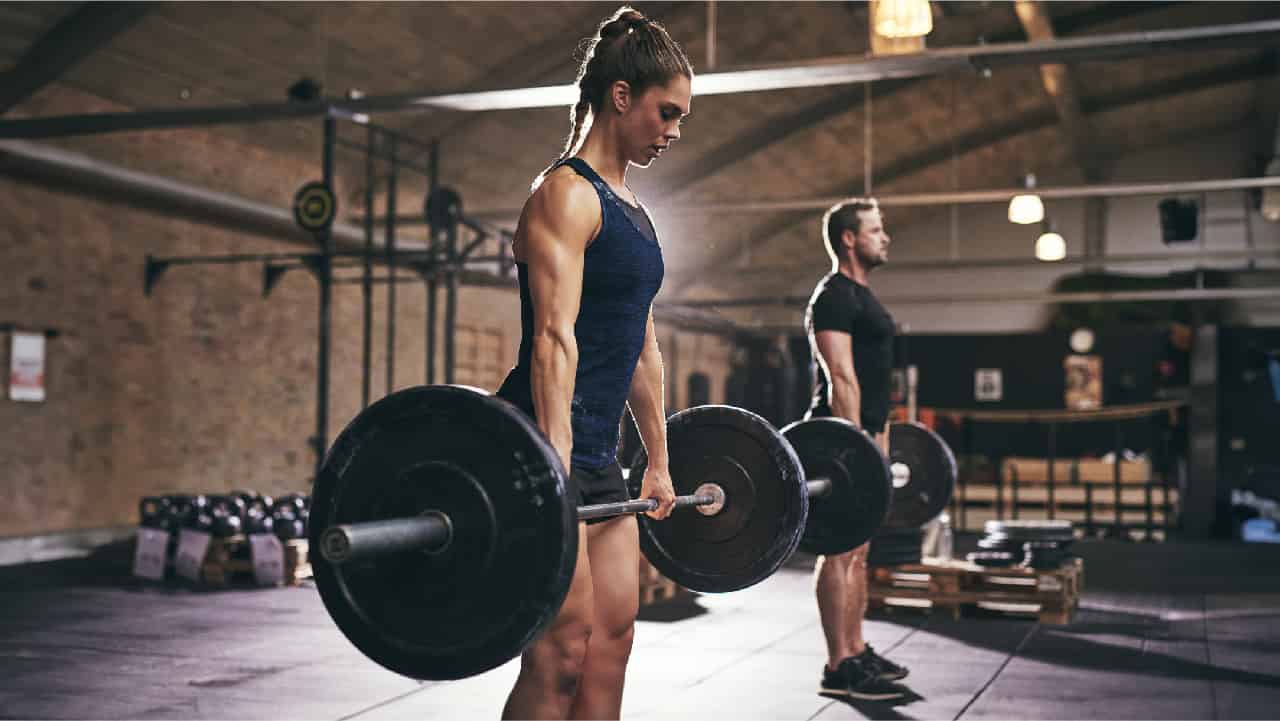 Woman and man in shorts working out in a gym with weights. The pros and cons of lifting on an 'empty stomach.'