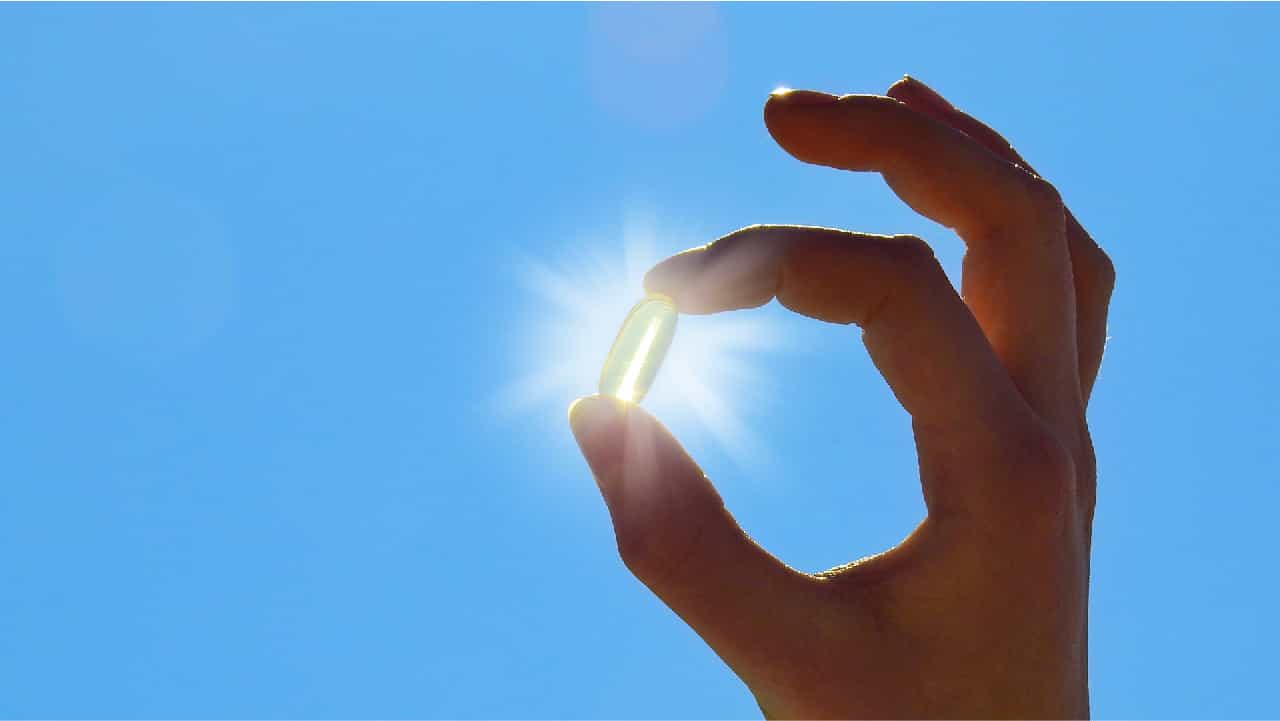 Hand holding a capsule up to the sun against a blue sky background