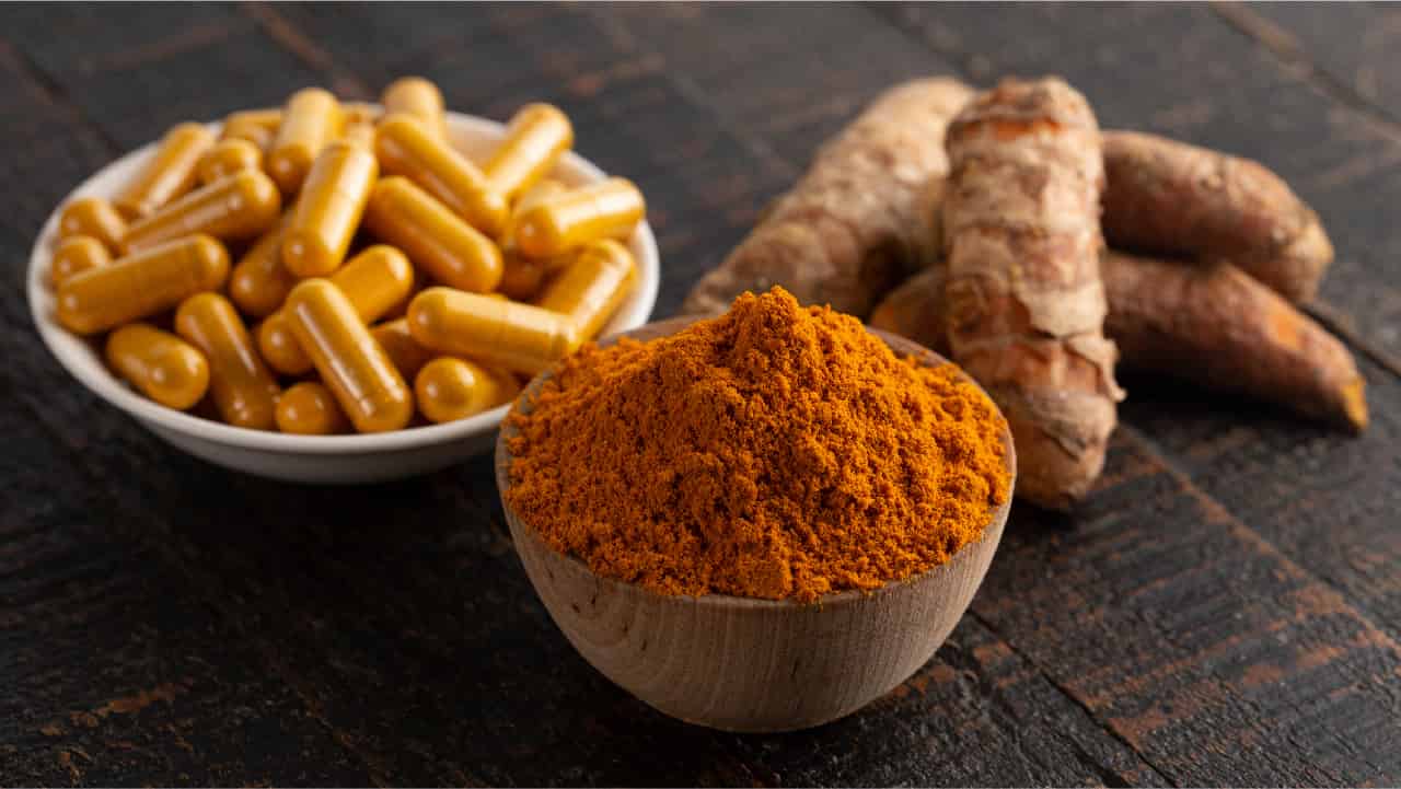 Bright orange turmeric root and powder form alongside a bowl of turmeric capsules