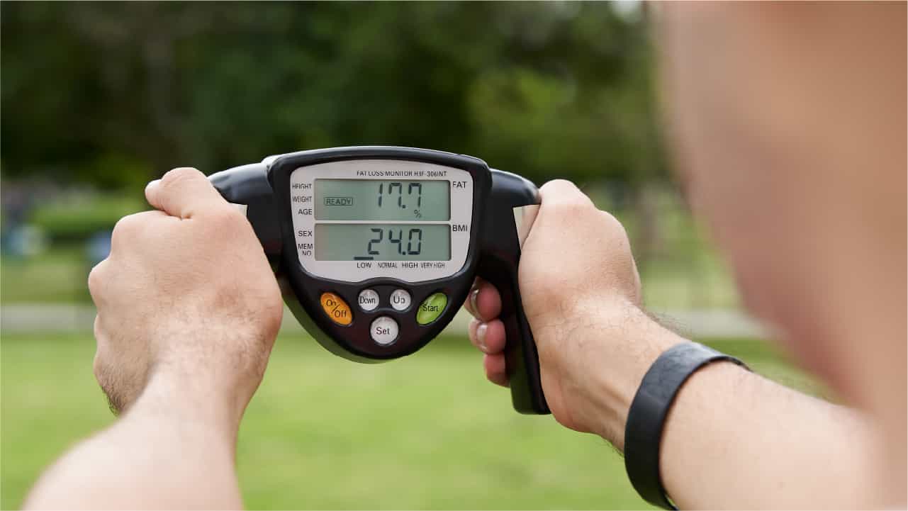 Man in a park holding a 'body fat' and BMI indicator