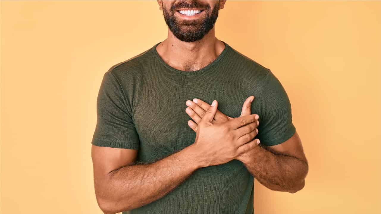 A man in a khaki green t-shirt with his hands over his heart. Concept that one of the health benefits of turmeric is it may support Cardiovascular Function