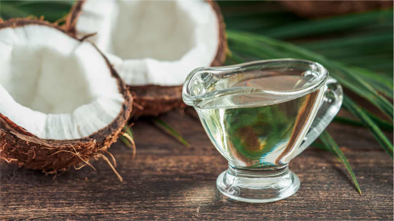 Coconut split in half next to a small glass pitcher filled with clean organic MCT oil, illustrating what to look for in a top MCT oil supplement.