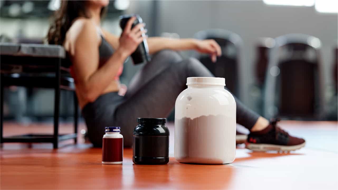 Woman sat on gym floor surrounded by 'creatine supplements'